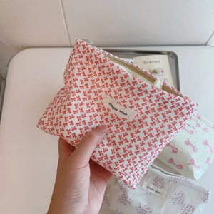 Handheld view of a cotton makeup bag featuring a sweet pink bow print and top zipper
