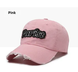 Detailed close-up of pink distressed baseball cap with Purist embroidery and ripped brim