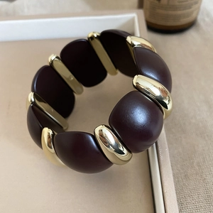 Macro detail of wine red acrylic and golden metal splicing bracelet on beige tray
