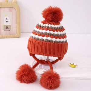 Detalle de gorro de punto para bebé con orejeras y tres pompones esponjosos naranja