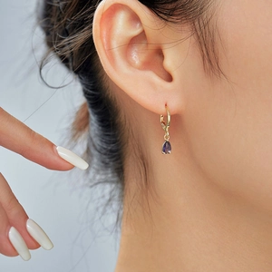 Macro shot of purple teardrop gemstone earrings with gold hoop on model's ear