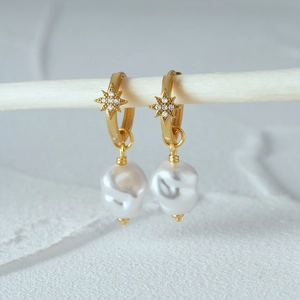Detail of star-engraved gold hoop earrings with white baroque pearl pendants
