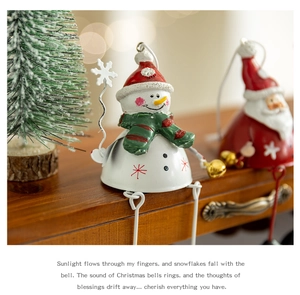 Detail view of a metal Christmas snowman bell ornament with a red hat and striped scarf