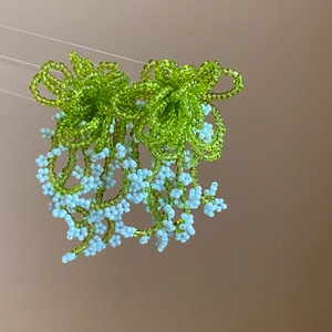 Detail of handmade beaded earrings with green flower cap and light blue tassel fringes