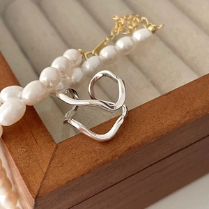 Macro shot of silver wavy irregular open ring on wooden box with white pearls