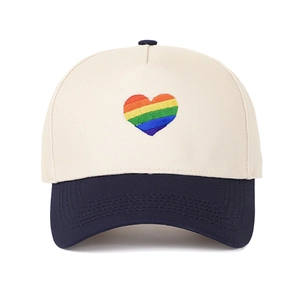 Dettaglio del ricamo a cuore arcobaleno su un cappellino da baseball bicolore beige