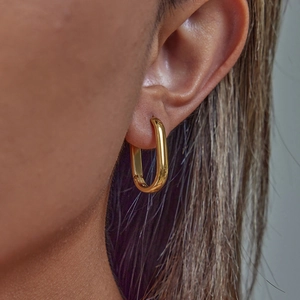 Close-up of a gold U-shaped stainless steel earring worn on a model's ear lobe