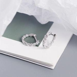Détail de boucles d'oreilles anneaux en argent S925 avec zircons sur un fond épuré
