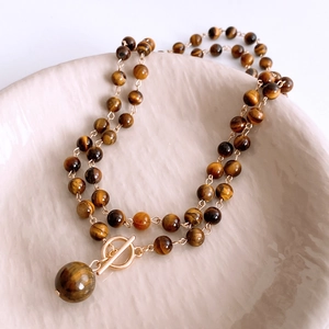 Detail of tiger eye stone necklace with gold toggle clasp on a ceramic tray