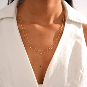 Detail of double-layered gold beaded necklace with oval beads on a model's neck