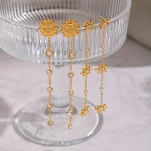 Elegant gold sun and star tassel earrings with zircon stones on a glass display stand
