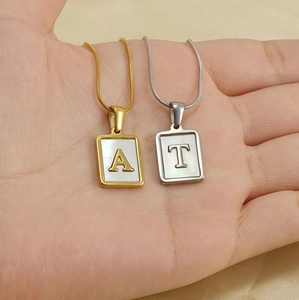 Détail de pendentifs carrés en nacre avec lettres A et T en or et argent sur chaînes fines