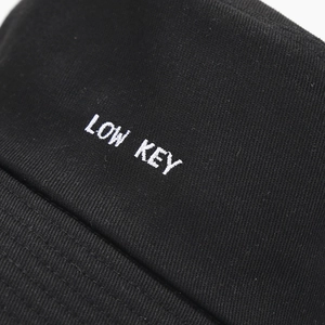 Black cotton bucket hat featuring white LOW KEY embroidery with premium twill texture