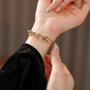 Close-up of stacked gold bracelets featuring colorful square zircon stones on model's wrist