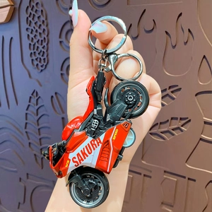 Cool red mini pull-back motorcycle keychain accessory held in hand over a textured background