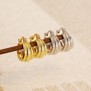 Macro shot of gold and silver triple-layered hoop earrings on a minimalist wooden stand