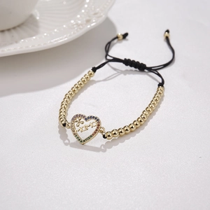Close-up of woven MAMA bracelet with gold heart charm and colorful crystals on grey surface
