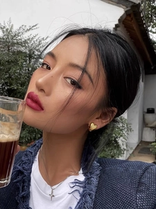 Close-up of model wearing gold heart earrings and star pendant necklace in outdoor setting