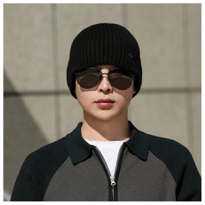 Close-up of black ribbed knit beanie with mountain logo on male model in industrial setting