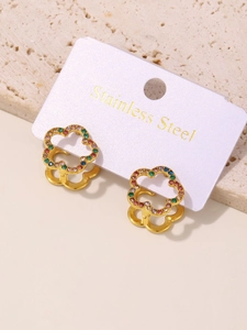 Detail view of flower-shaped gold earrings with colorful rhinestones on a stone surface