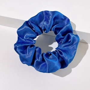 Detailed view of a bright blue satin scrunchie on a white minimalist geometric step