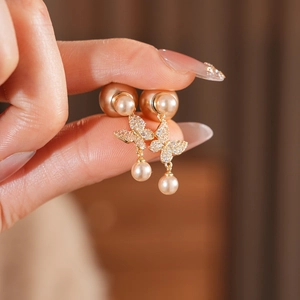 Detailed close-up of gold butterfly pearl earrings with sparkling micro-pave crystals