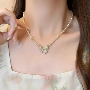 Elegant pearl choker necklace with gold crystal bow pendant worn by a model