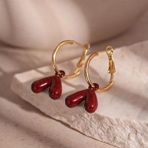 Close-up of vintage deep red heart earrings with golden hoops on a textured stone base