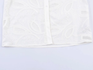 Detail of white embroidered shirt showing intricate floral cut-out patterns and fabric texture