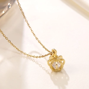 Elegant gold crown pendant necklace with sparkling zircon stone on a white surface