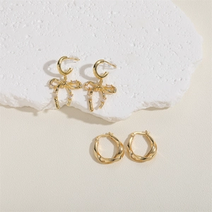 Detail of luxury gold earrings with crystal bow knot and polished twisted metal hoop