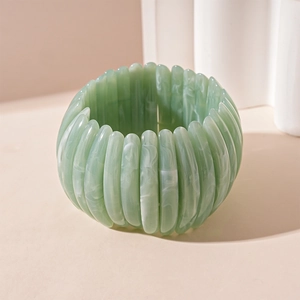 Détail du bracelet en résine marbrée vert clair au design segmenté sur fond neutre
