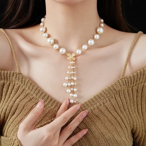 Detailed view of the white faux pearl necklace with gold clover and tassel pendant on a model