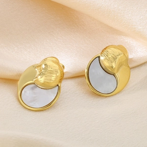 Macro shot of gold-rimmed white shell earrings on champagne satin fabric background