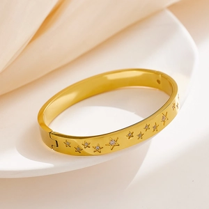 Detailed view of a gold star-engraved stainless steel bangle on a white ceramic plate