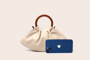 Beige cloud handbag with wooden circular handle showing phone size comparison