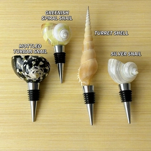 Detailed view of four decorative conch seashell wine stoppers with stainless steel bases