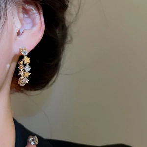 Close-up of a sparkling gold star and zircon C-shaped earring worn on a model's ear