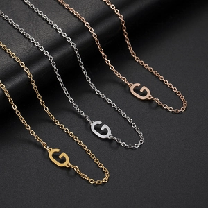 Detailed view of three stainless steel necklaces with G pendants in gold, silver, rose gold