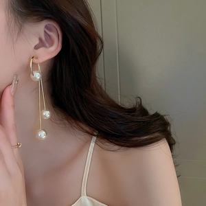 Detail of elegant gold tassel earrings with three pearls on a female model
