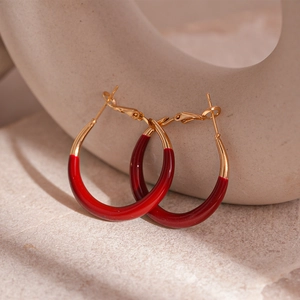 Close-up of C-shaped burgundy enamel gold hoop earrings on a stone textured stand