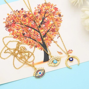 Three gold evil eye necklace pendants with moon, lash, and crown designs on blue background