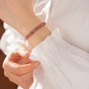 Detail of pink strawberry crystal beaded bracelet worn on wrist with white fabric backdrop