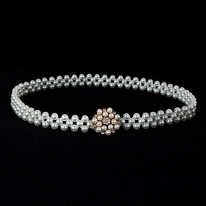 Detail view of white pearl belt featuring a gold rhinestone buckle on black background