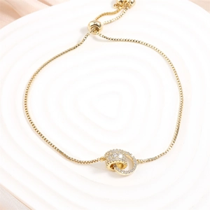 Dettaglio macro di un bracciale dorato a doppio anello con micro-pavé di zirconi e catena
