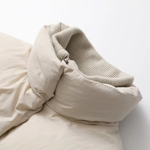 Detail view of the beige winter jacket showing knit ribbed collar and polyester shell texture