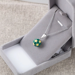 Macro detail of 3D yellow and green soccer pendant necklace on a gray velvet display box