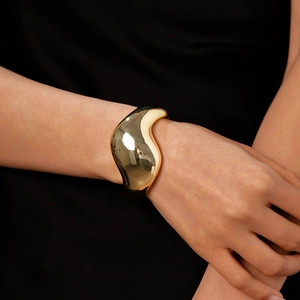 Poliertes goldfarbenes Armband in unregelmäßiger Form am Model vor Schwarz