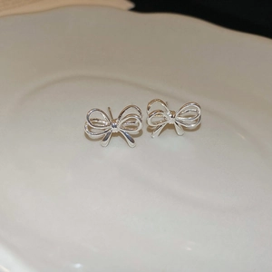 Detailed macro view of silver bow stud earrings on a white decorative ceramic plate