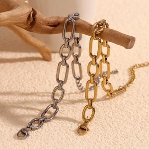 Détail des bracelets à maillons trombone épais en or 14K et argent sur une branche de bois